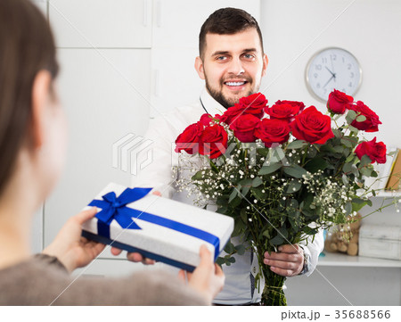 Positive young guy presenting bouquet and gift Positive young guy presenting bouquet and gift 35688566