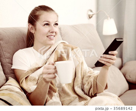 Girl is resting with tea in plaide and watching TV Girl is resting with tea in plaide and watching TV 35689142