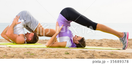 Young couple doing yoga poses sitting on sunny beach 35689378