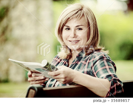 Portrait of mature woman sitting on bench and reading book in garden Portrait of mature woman sitting on bench and reading book in garden 35689857