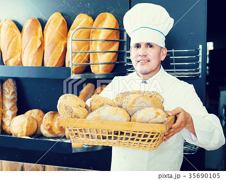Male employee offering fresh baguettes and buns in bakery 35690105