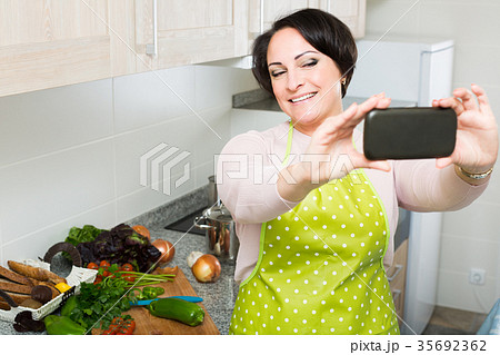 Portrait of housewife in apron making selfie in domestic kitchen 35692362