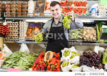 positive male seller showing assortment of grocery shop 35692506