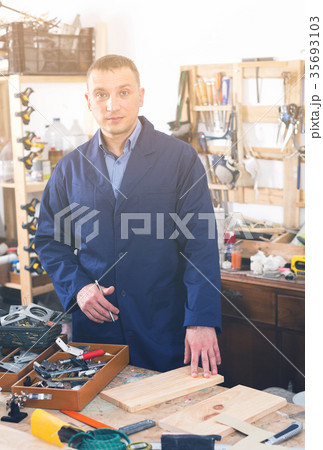 Portrait of happy young handsome carpenter in uniform in workshop. 35693103
