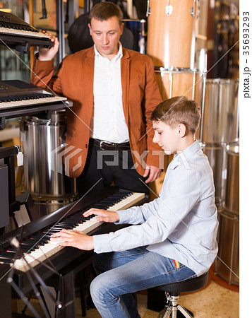 Father and teenage son examining keyboards in guitar shop 35693293