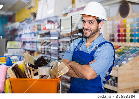 Workman standing folded arms near basket with picked tools in paint store Workman standing folded arms near basket with picked tools in paint store 35693384