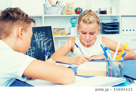 Boy with girl are writing in notebook their homework Boy with girl are writing in notebook their homework 35694315