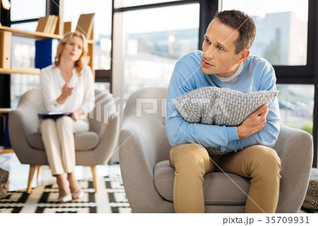 Unhappy cheerless man holding a pillow Unhappy cheerless man holding a pillow 35709931