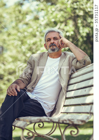 Pensive mature man sitting on bench in an urban park. Pensive mature man sitting on bench in an urban park. 35731117