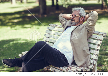 Pensive mature man sitting on bench in an urban park. Pensive mature man sitting on bench in an urban park. 35731118