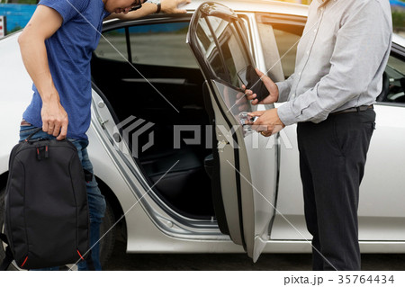 Taxi driver greeting his passengers with their luggage on the si 35764434