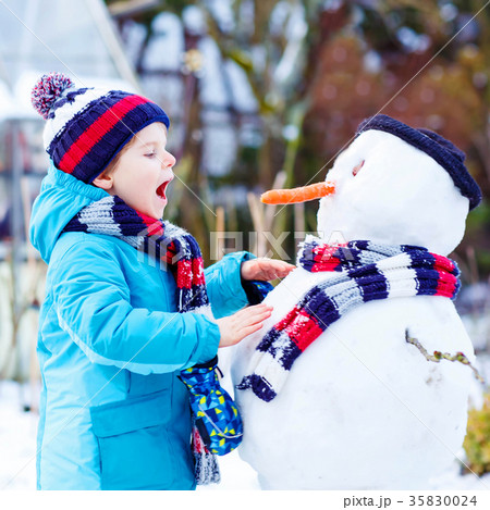 Funny kid boy in colorful clothes making a snowman 35830024