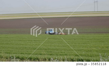 Blue wheeled tractor plowing a green field Blue wheeled tractor plowing a green field 35852118