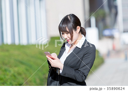 スマホを持ったスーツの女性　OL　ビジネス　スーツ　ポートレート　リクルート　緑背景　 35890624
