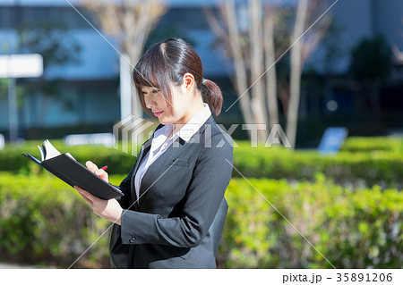 手帖を持ったスーツの女性　OL　ビジネス　スーツ　ポートレート　リクルート　緑背景　 35891206