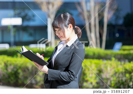 手帖を持ったスーツの女性　OL　ビジネス　スーツ　ポートレート　リクルート　緑背景　 35891207