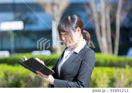 手帖を持ったスーツの女性　OL　ビジネス　スーツ　ポートレート　リクルート　緑背景　 35891211