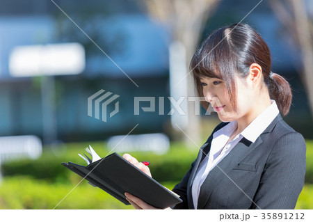 手帖を持ったスーツの女性　OL　ビジネス　スーツ　ポートレート　リクルート　緑背景　 35891212