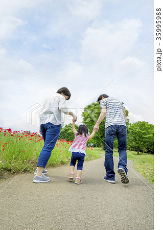 花の咲く新緑の公園で遊ぶ3人家族の後ろ姿の写真素材