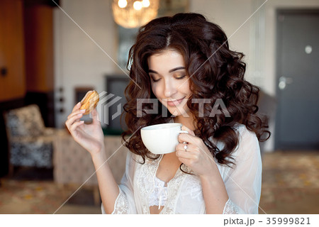 Woman holding a cup of coffee and a donut at home 35999821