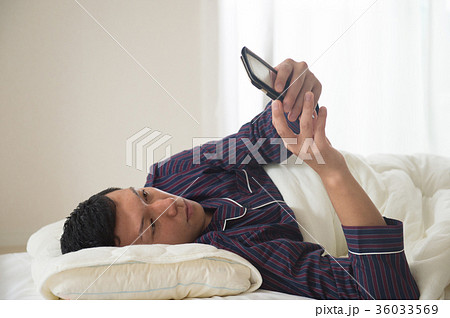 ベッドでスマホを見る若い男性 36033569