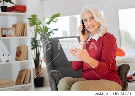 Beaming retired woman talking on phone and using 36043573