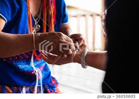 Unidentified elder woman from Karen ethnic hill tribe minority tie guest's wrist for blessing in tying ceremony 36050605