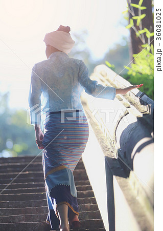 Portrait of thai young woman with traditional thai dress walking in thai temple with tree and sunrise 36081025