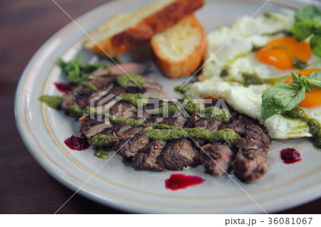 Grilled beef steak with toast , fried egg and vegetables on top with pesto sauce 36081067