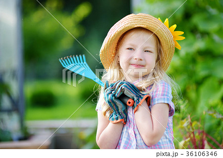Adorable little girl wearing straw hat and childrens garden gloves playing with her toy garden tools 36106346