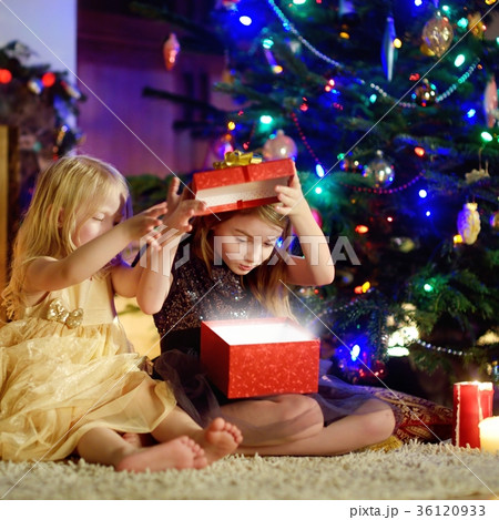 Happy little sisters opening magical Christmas gift by a fireplace 36120933
