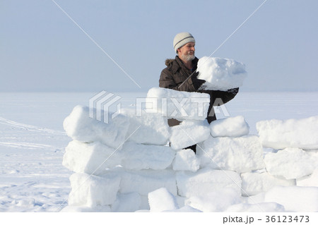 Man with a beard in a gray cap building an igloo Man with a beard in a gray cap building an igloo 36123473