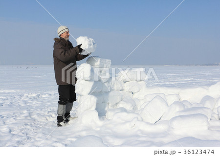 Man with a beard in a gray cap building an igloo Man with a beard in a gray cap building an igloo 36123474