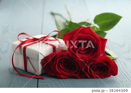 three red roses on blue wood table with gift box 36164309
