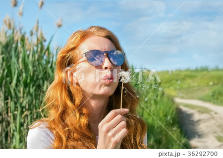 red-haired girl in sunglasses blows away dandelion 36292700