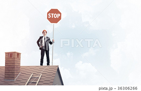 Caucasian businessman on brick house roof showing stop road sign Caucasian businessman on brick house roof showing stop road sign 36306266