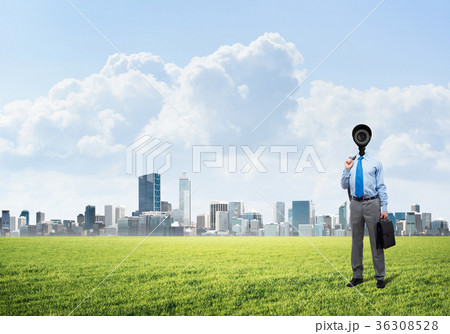 Camera headed man standing on green grass against modern cityscape 36308528