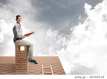 Handsome man on brick roof against cloud scape reading book 36308529