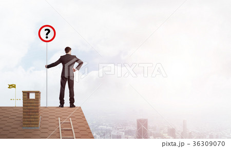 Businessman on brick house roof showing banner with question mark. Mixed media Businessman on brick house roof showing banner with question mark. Mixed media 36309070