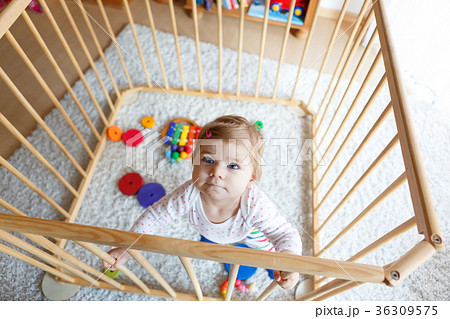 Beautiful little baby girl standing inside playpen 36309575