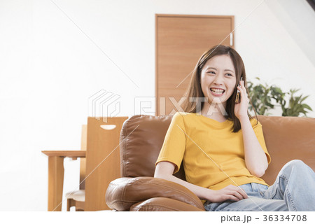 自宅リビングのソファーで携帯電話をする若い女性 自宅リビングのソファーで携帯電話をする若い女性 36334708