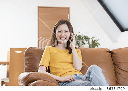 自宅リビングのソファーで携帯電話をする若い女性 自宅リビングのソファーで携帯電話をする若い女性 36334709
