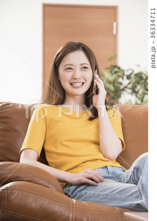自宅リビングのソファーで携帯電話をする若い女性 自宅リビングのソファーで携帯電話をする若い女性 36334711
