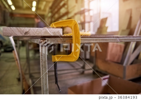 C-clamp is clamping a metal plate to a table. C-clamp is clamping a metal plate to a table. 36384193