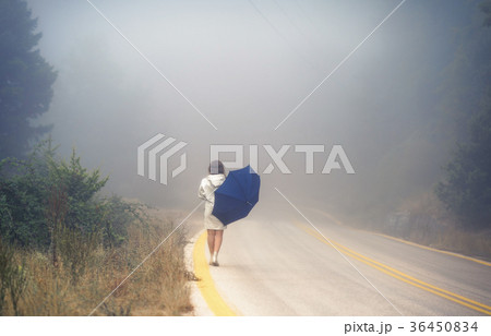 female in a raincoat and umbrella on the road 36450834