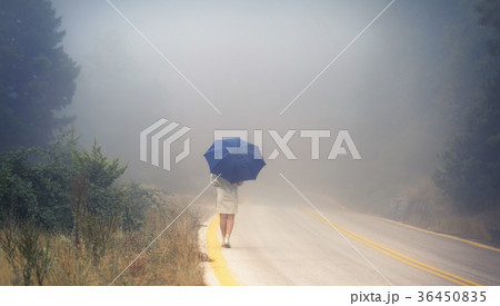 female in a raincoat and umbrella on the road 36450835