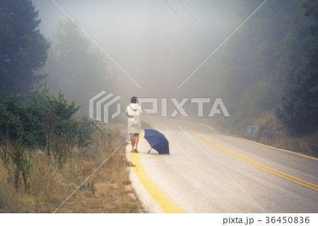 female in a raincoat and umbrella on the road 36450836