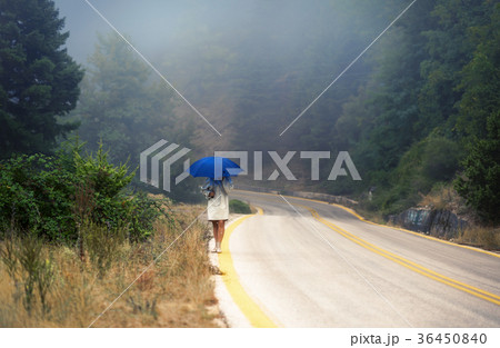 female in a raincoat and umbrella on the road 36450840