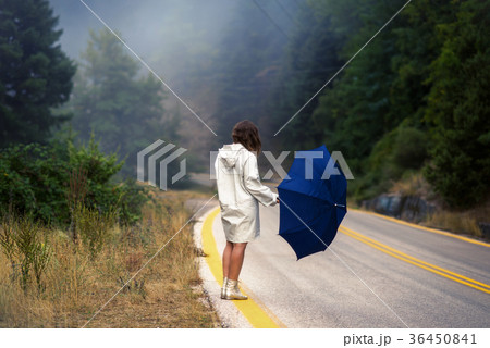 female in a raincoat and umbrella on the road 36450841