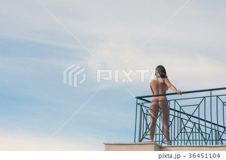 Naked female with camera on balcony opposite sky  36451104